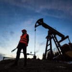 Oil pump jack silhouetted against a colourful evening sky.