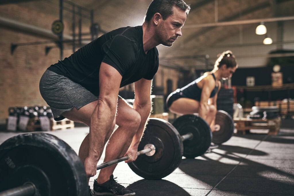 Man performing deadlift with barbell in gym setting.